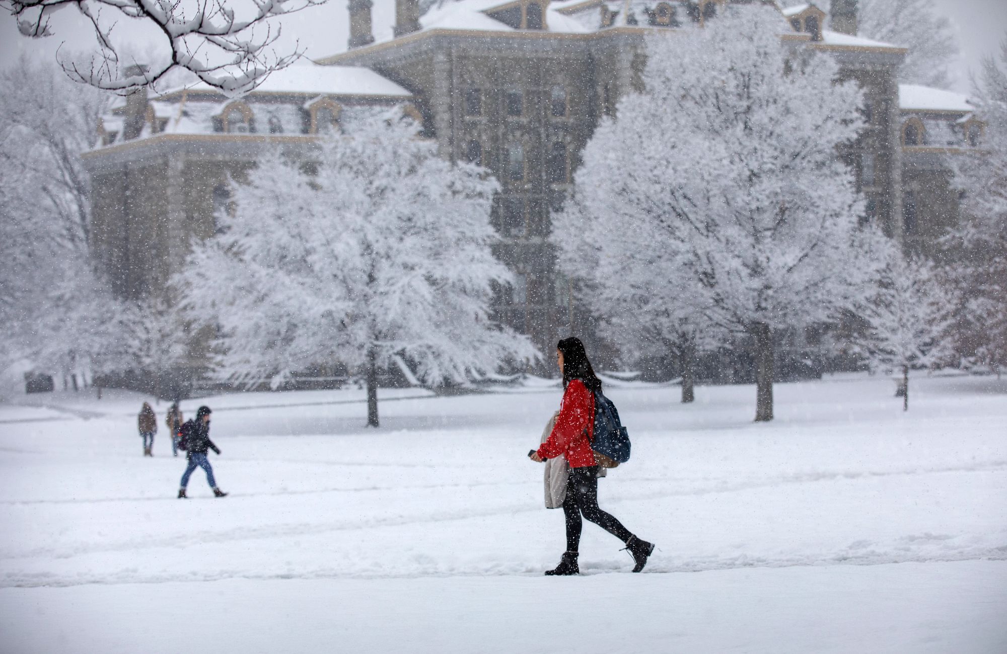 A Cornell student wearing a red coat walking across the Arts Quad in the snow.